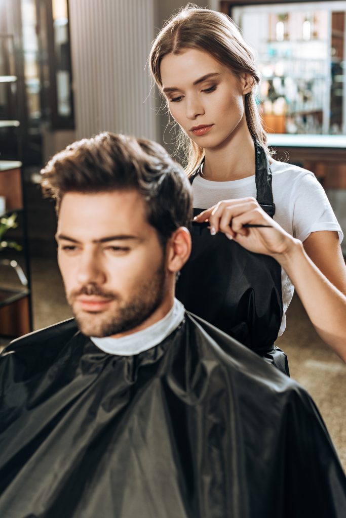 young hairdresser combing hair to handsome man in beauty salon